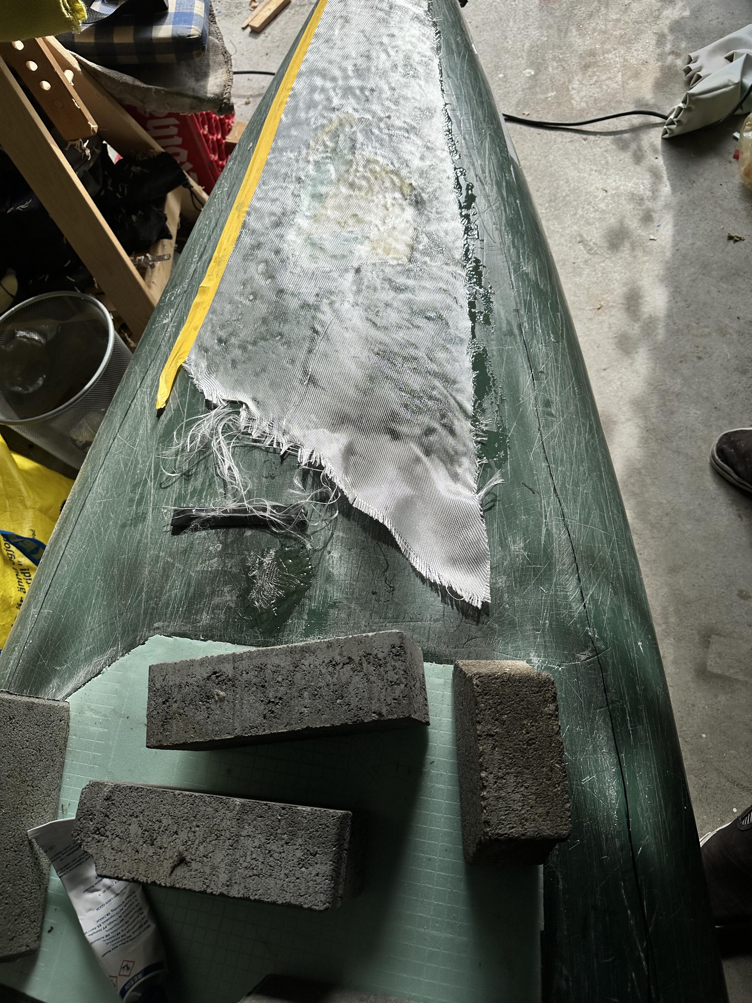 At the lower end is the fix with the foam board glued in. Stones are on the board to keep it down. At the top of the image a piece of glass fabric is wetted with g-flex epoxy.